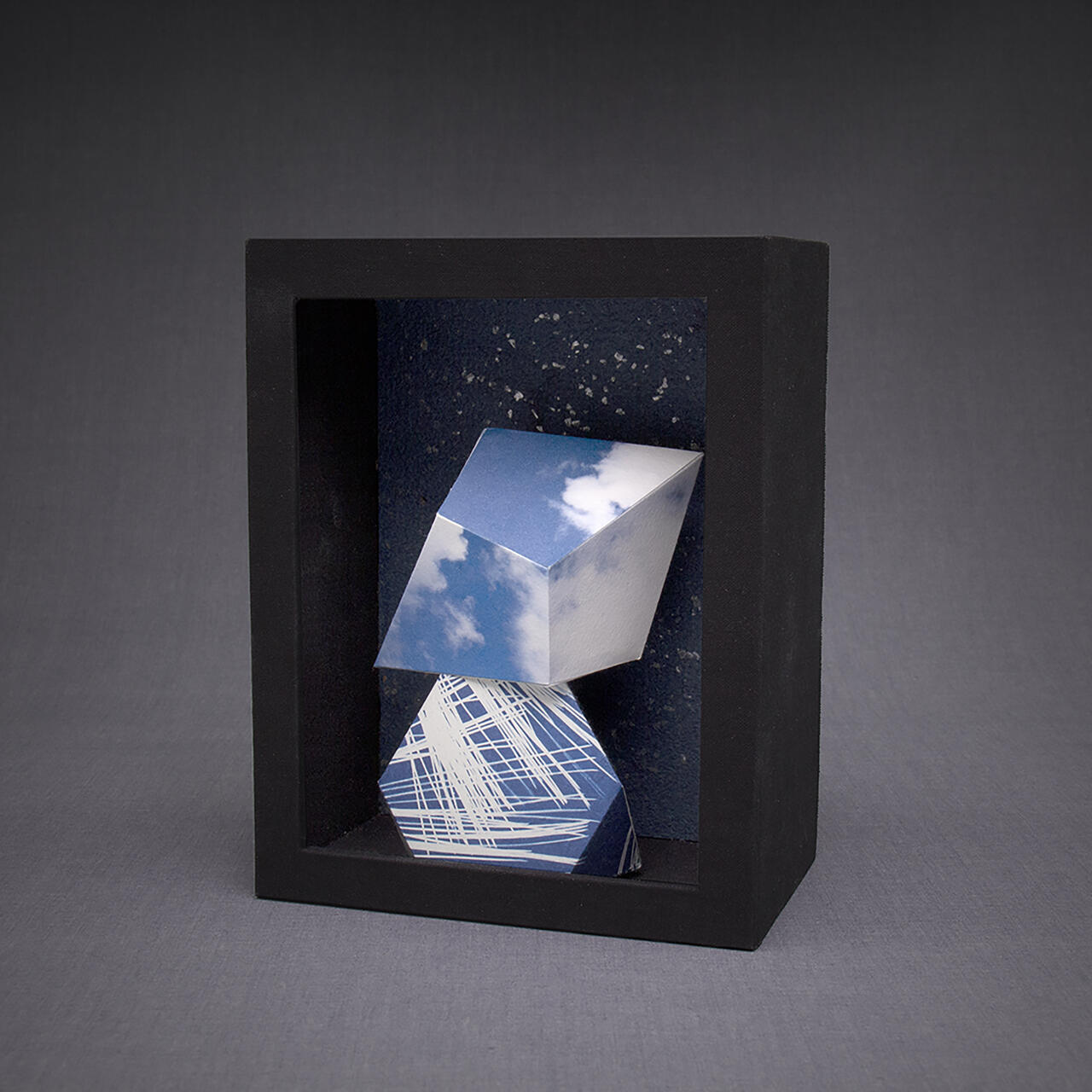 An image showcasing a framed box with two geometric cyanotype objects inside.