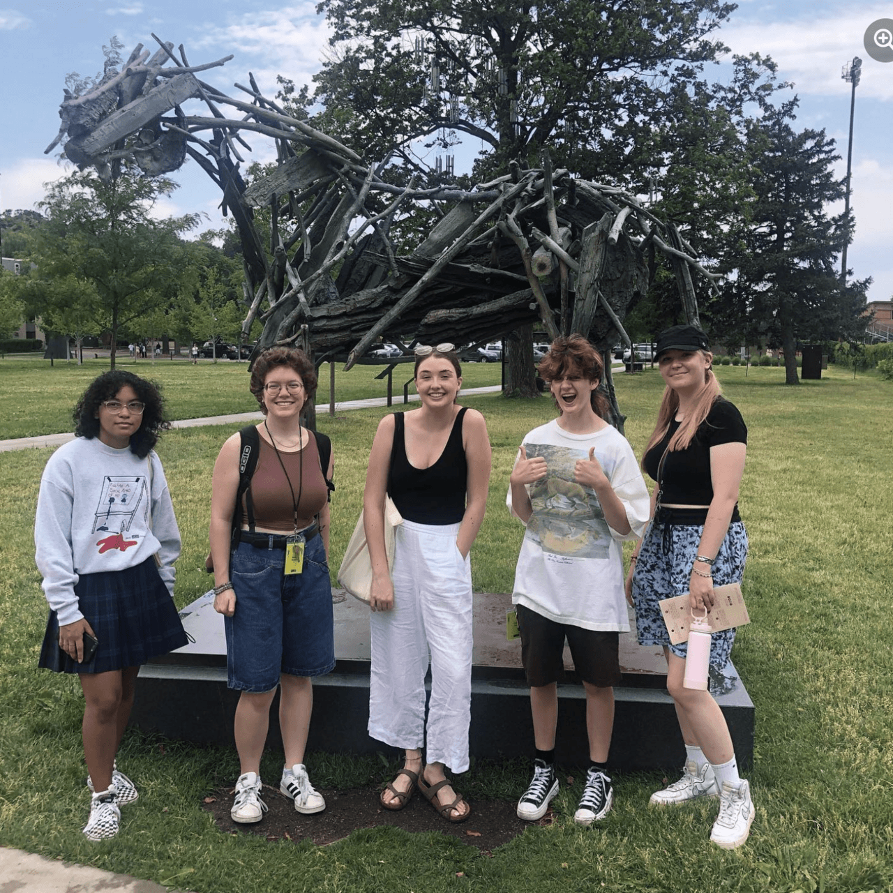 Group of five students stand outside in front of an abstract horse sculpture made out of pieces of wood.