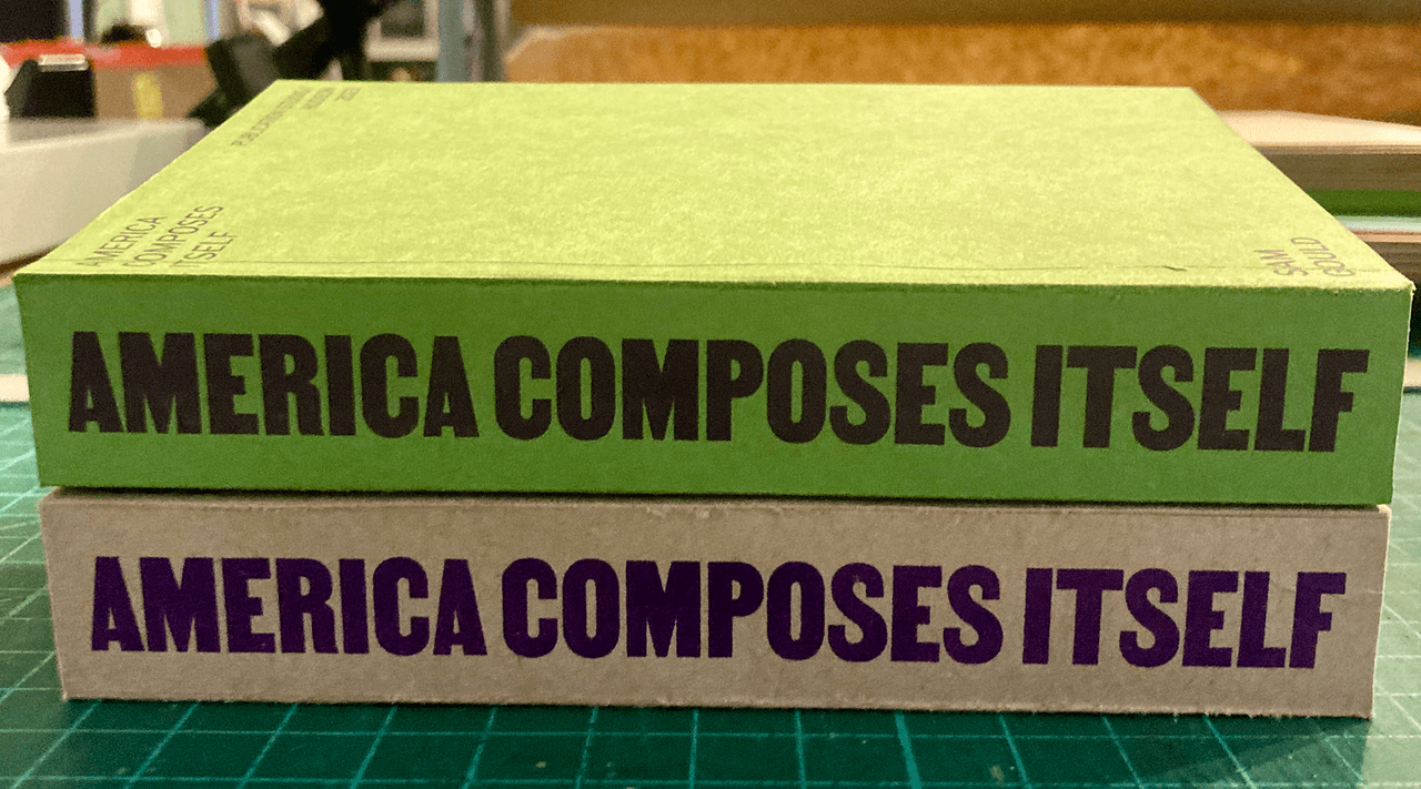 Two copies of the book America Composes Itself stacked on a table.