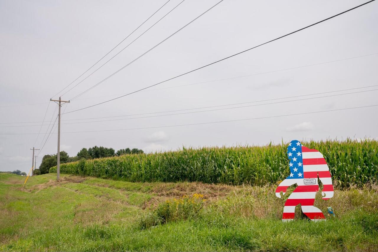 A shot of a corn field with a cut out of big foot in front of it. The big foot is painted as the United States flag.
