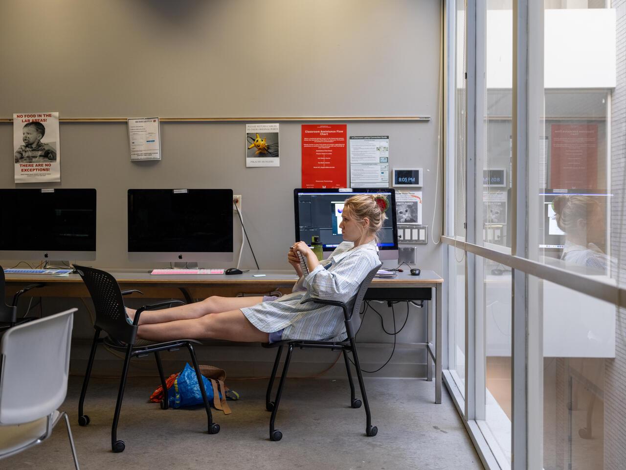 Graphic Design Minor Hero Image: CE photography of a student sitting on a chair in an MCAD mac lab