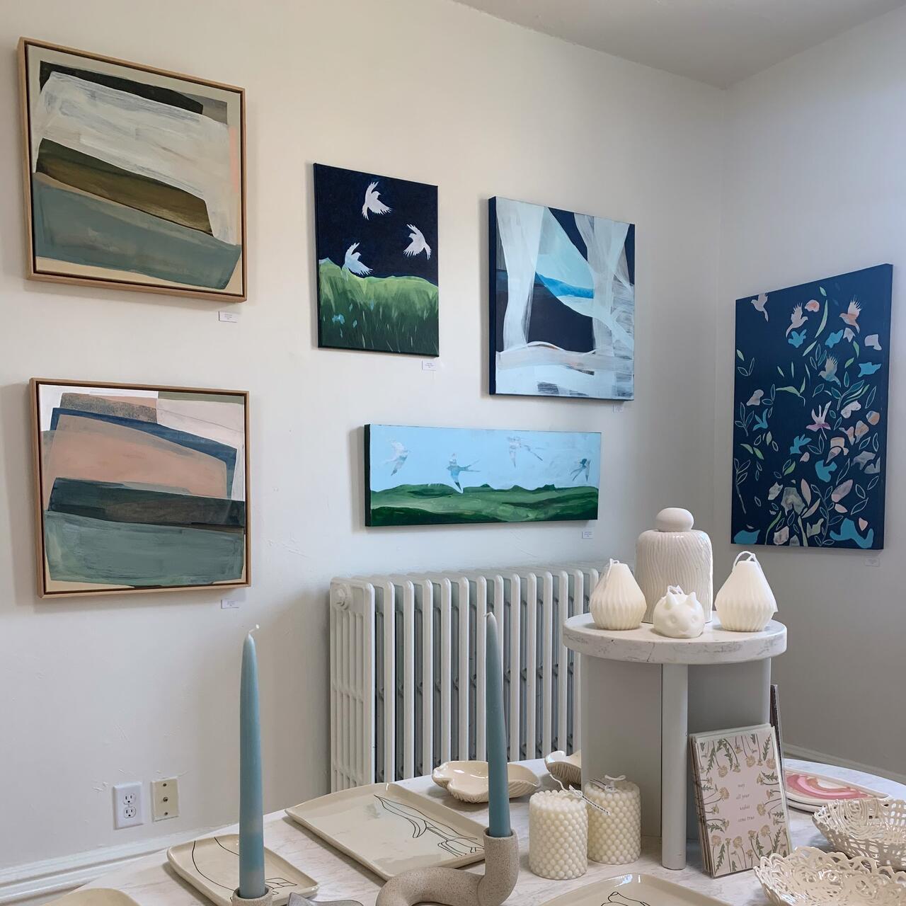 A photo of the inside of Collected Gallery. There's a small table with various candles and ceramics, as well as paintings on the wall.
