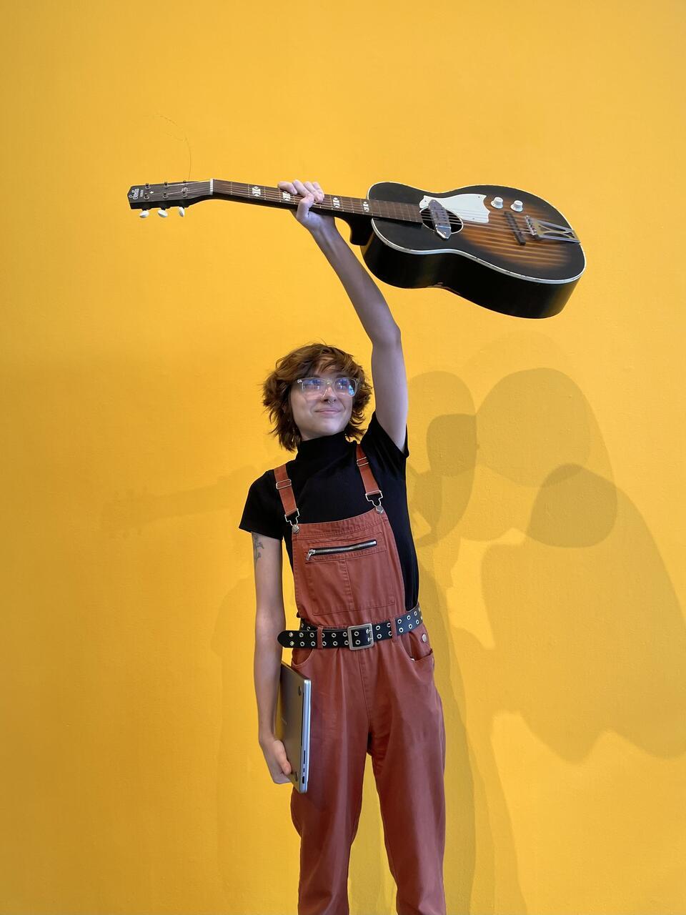 Sound minor image, student holding up a guitar with a yellow background