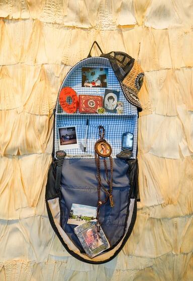 Juan's Backpack by Graciela DeAnda. The work features a backpack with various memorial items in it.
