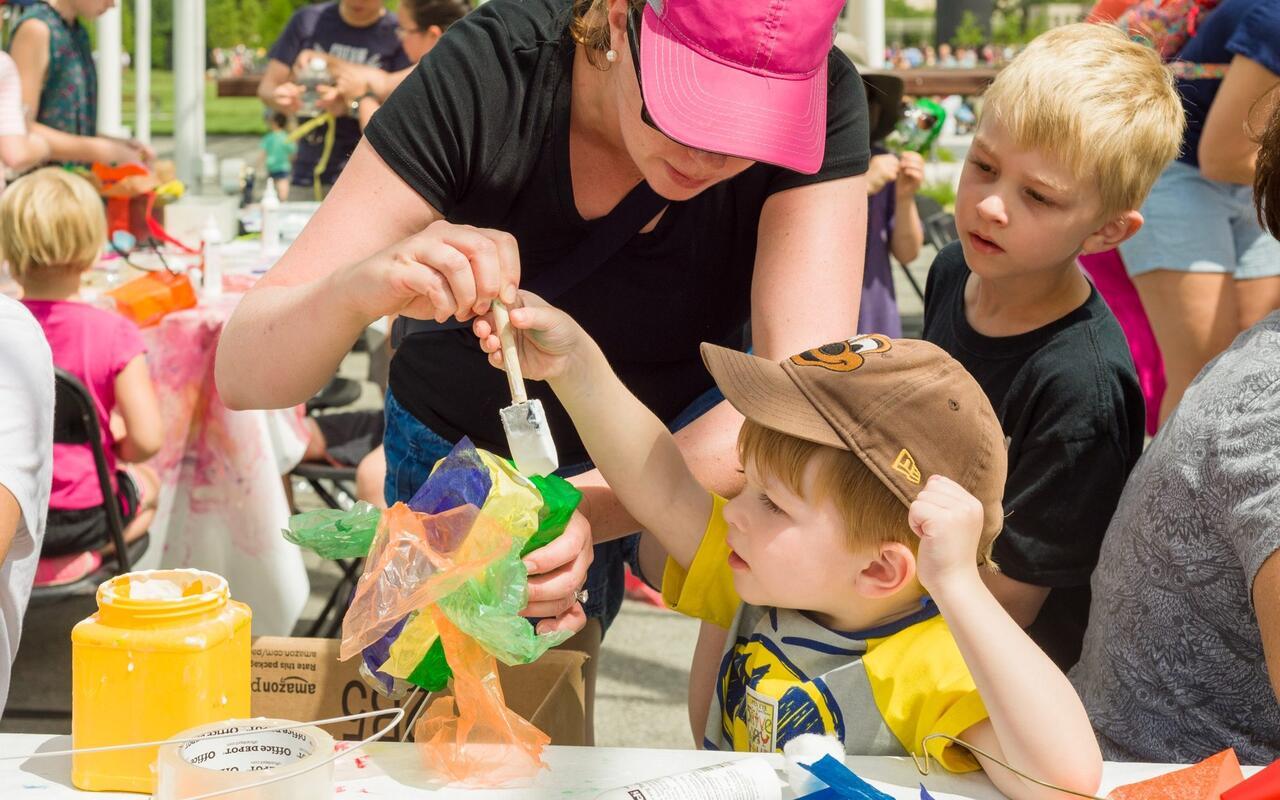 A promotional imae for the Walker's Garden Play Party. The image features a young child creating a craft with and older adult in a pink baseball cap.